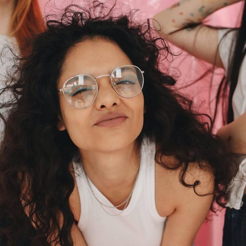 a girl in white tank top smiling while wearing eyeglasses